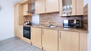 Een moderne keuken met houten kastjes, een roestvrijstalen spoelbak, een magnetron en een ingebouwde oven.