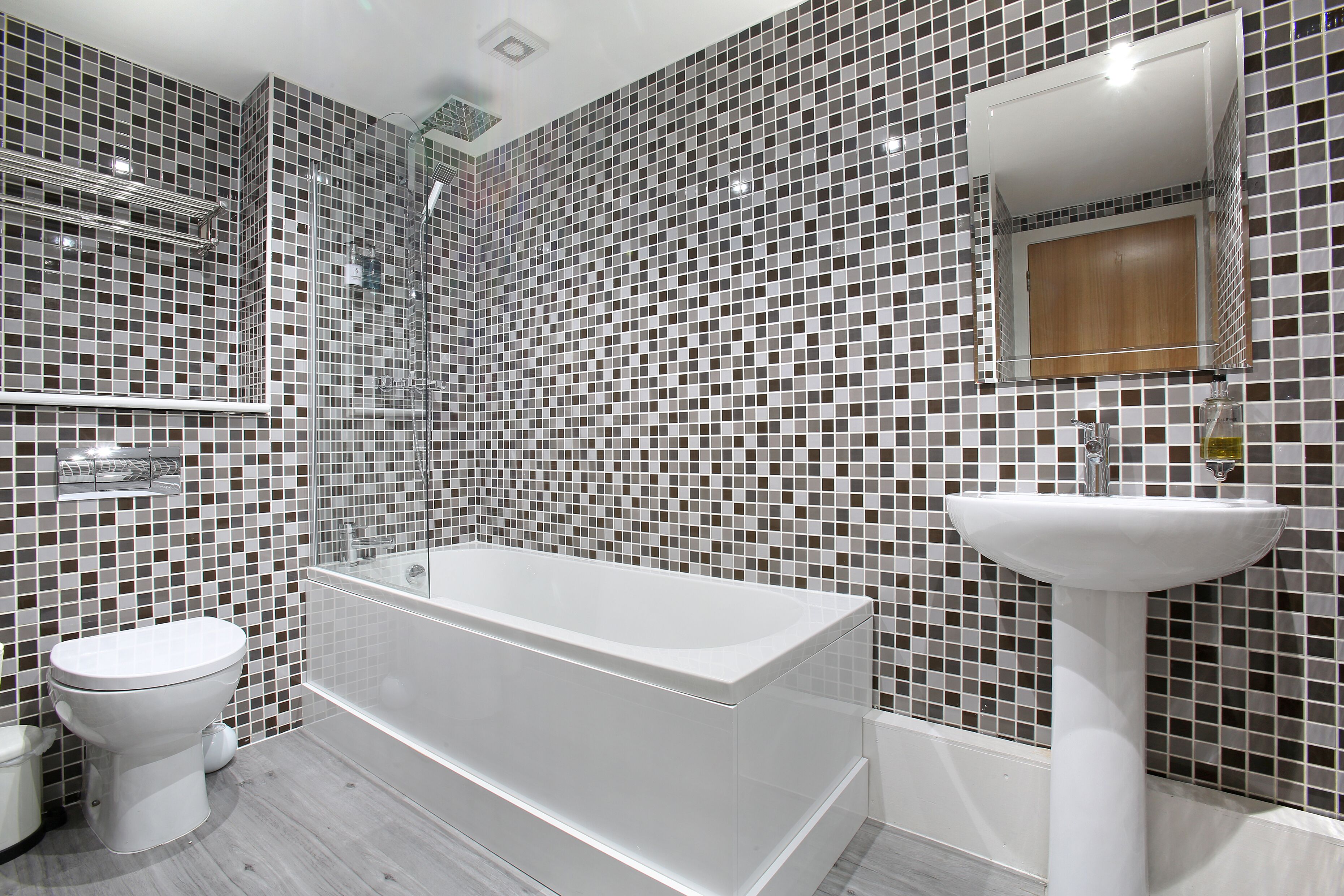 A modern bathroom with a white bathtub, a white sink, and a toilet. The walls are covered with mosaic tiles.