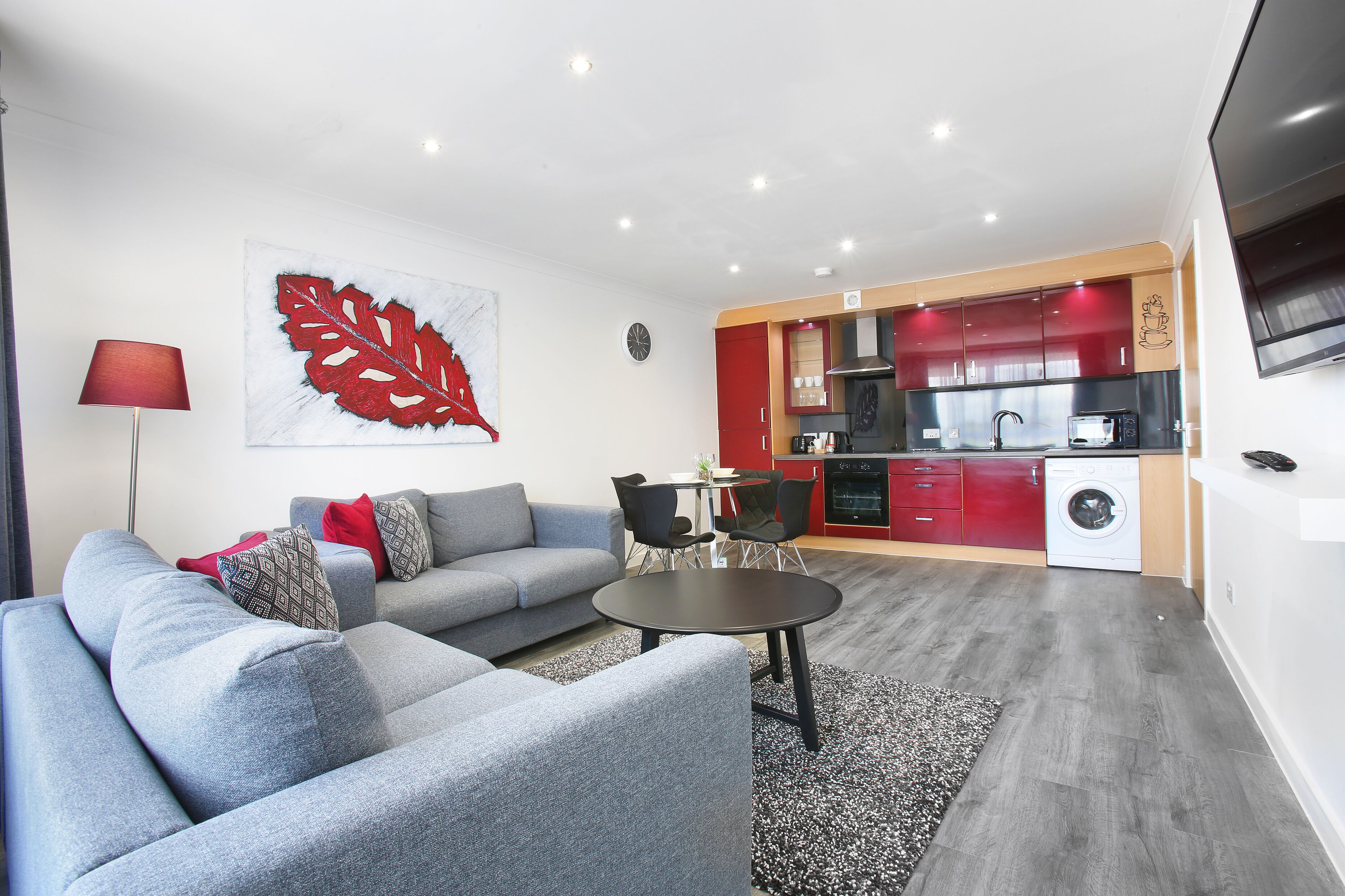 Una sala de estar moderna con un sofá gris, una mesa de centro redonda y un cuadro abstracto rojo en la pared.