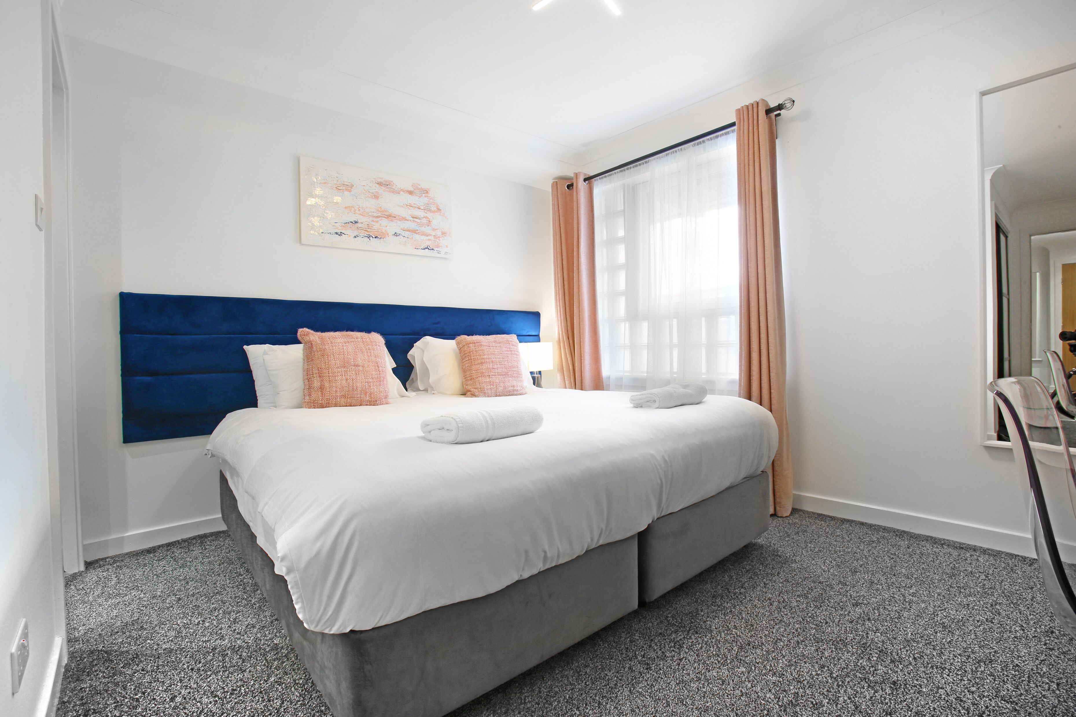 A hotel room with a large bed, a blue headboard, and a window with curtains.