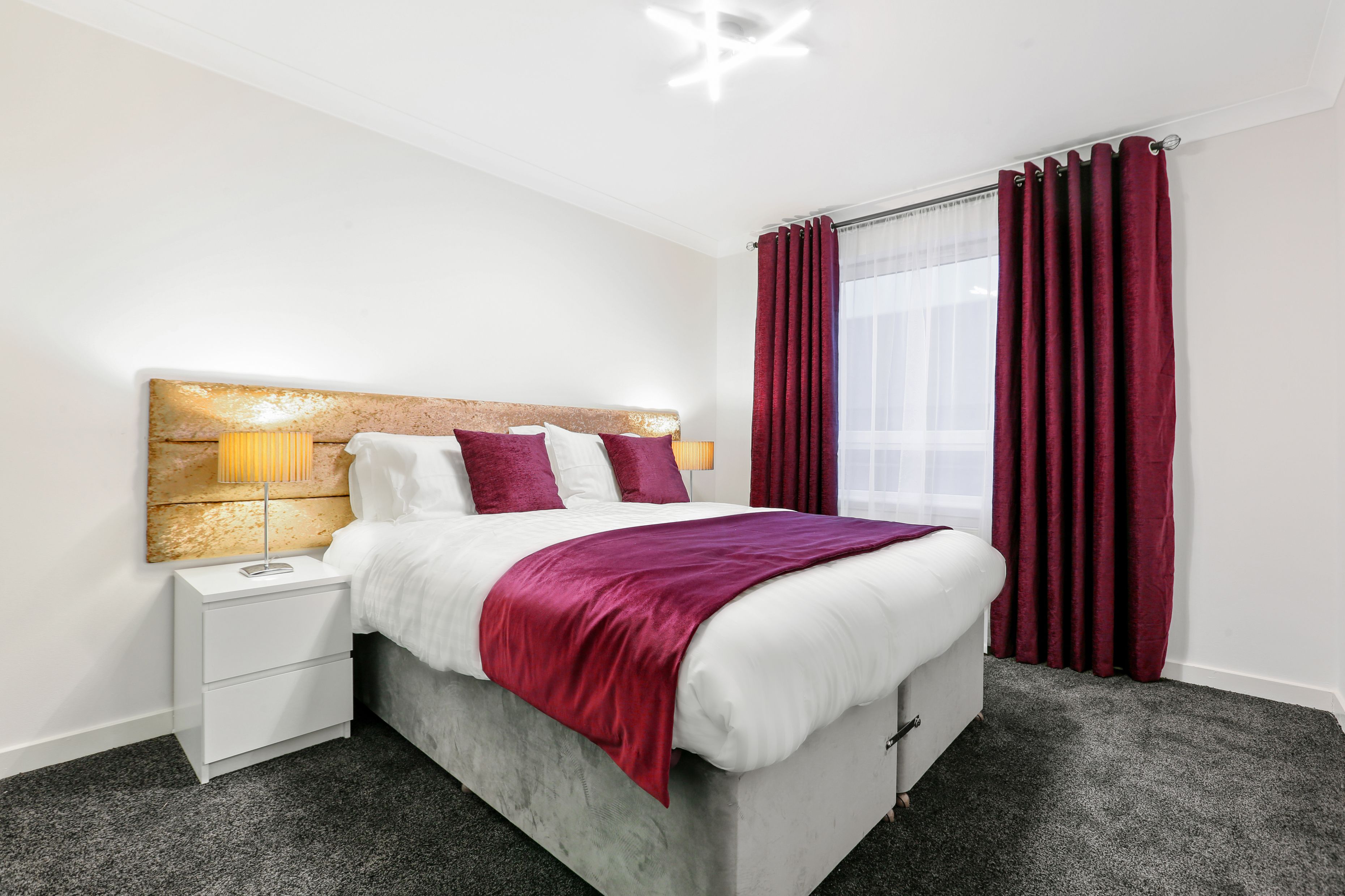 A neatly arranged bedroom with a bed, nightstand, lamp, and curtains.