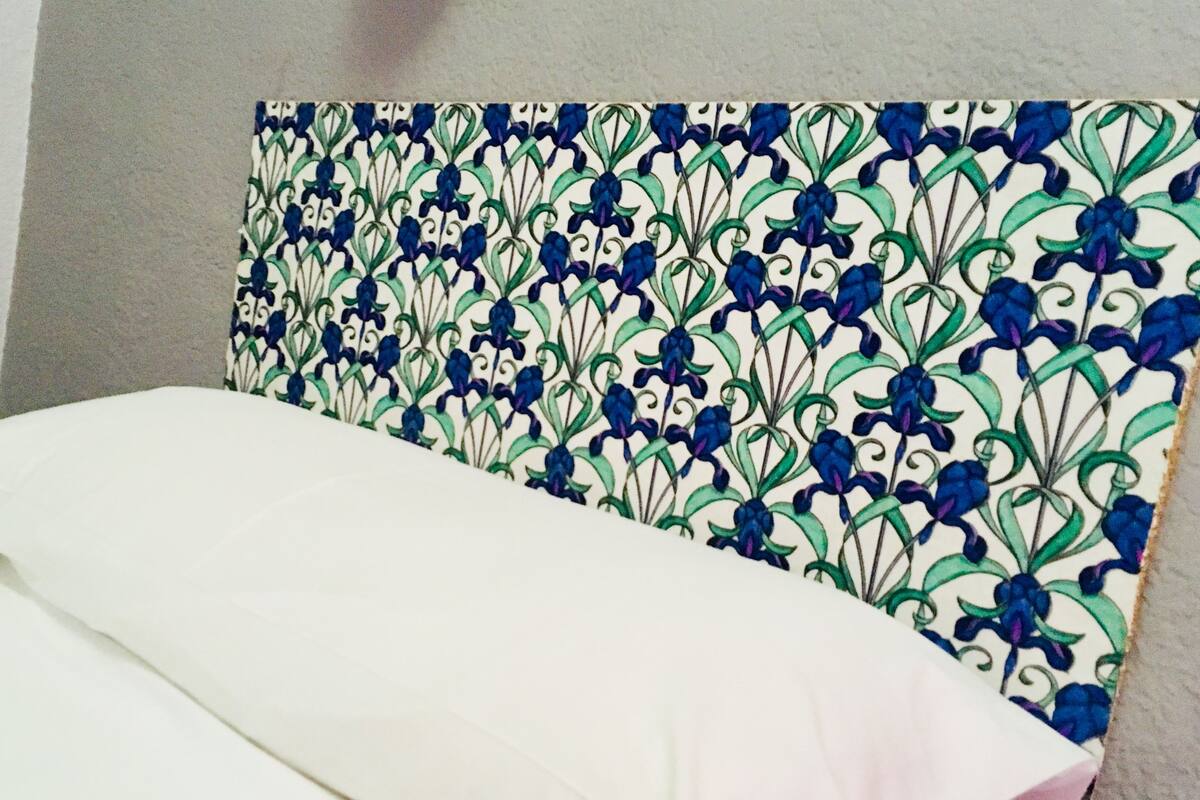 A bed with a white sheet and a headboard with a blue and green floral pattern.