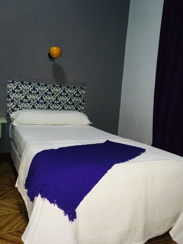 Una cama individual con un edredón blanco y morado, un cabecero estampado y una pared lisa.