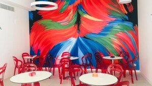 A modern interior with red chairs and white tables, a colorful abstract mural on the wall, and circular ceiling lights. - Nuevo Tropical (Motril)