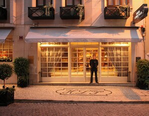Fachada de hotel de vidrio amplia, un hombre de pie frente a ella y adoquinado.