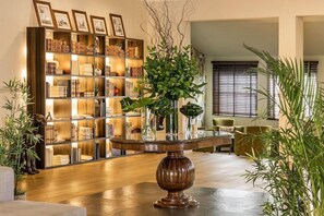Una habitación bien iluminada con una estantería de madera, una mesa redonda y varias plantas.