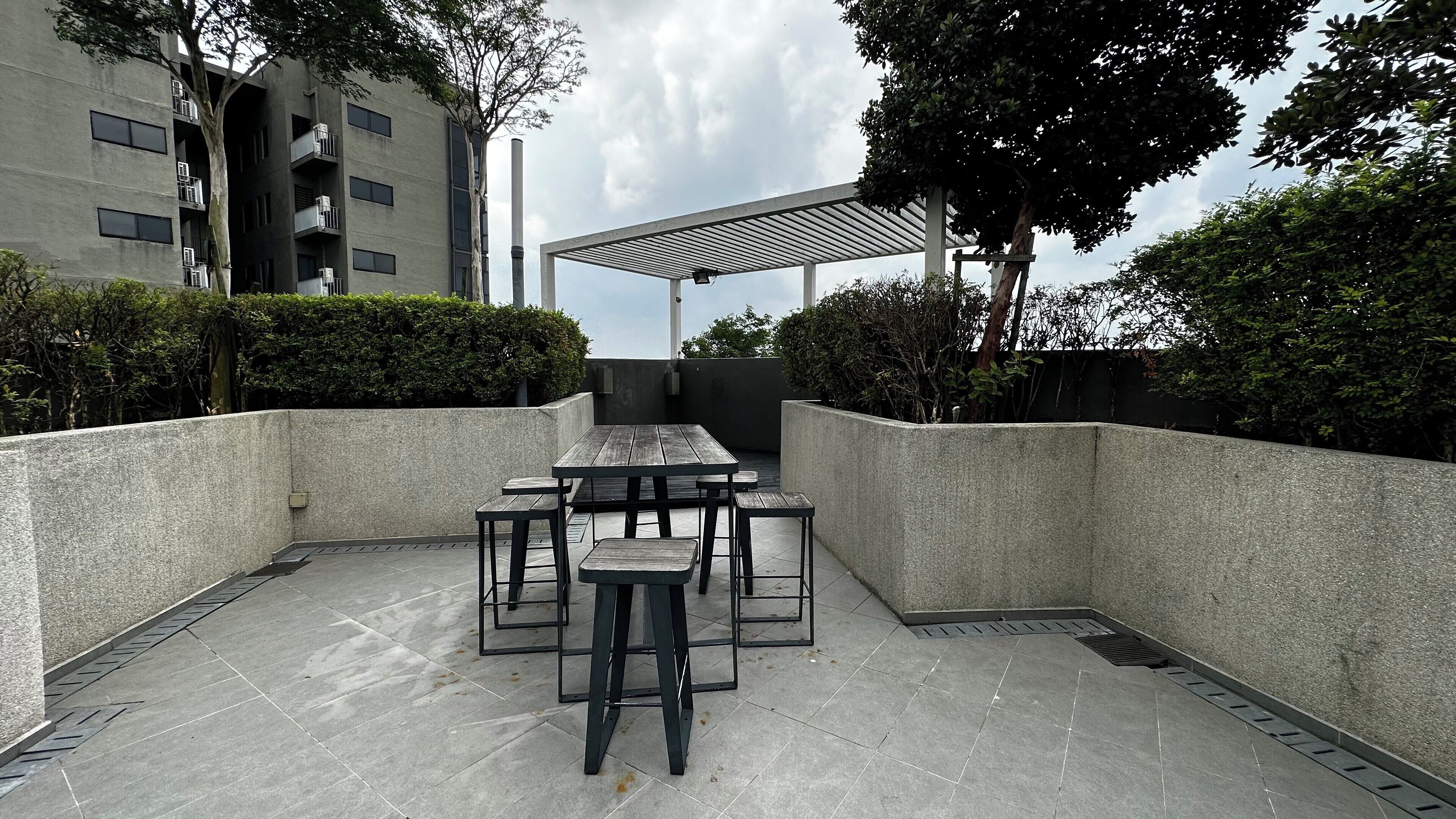 An outdoor patio with a table and chairs, surrounded by low stone walls and greenery.