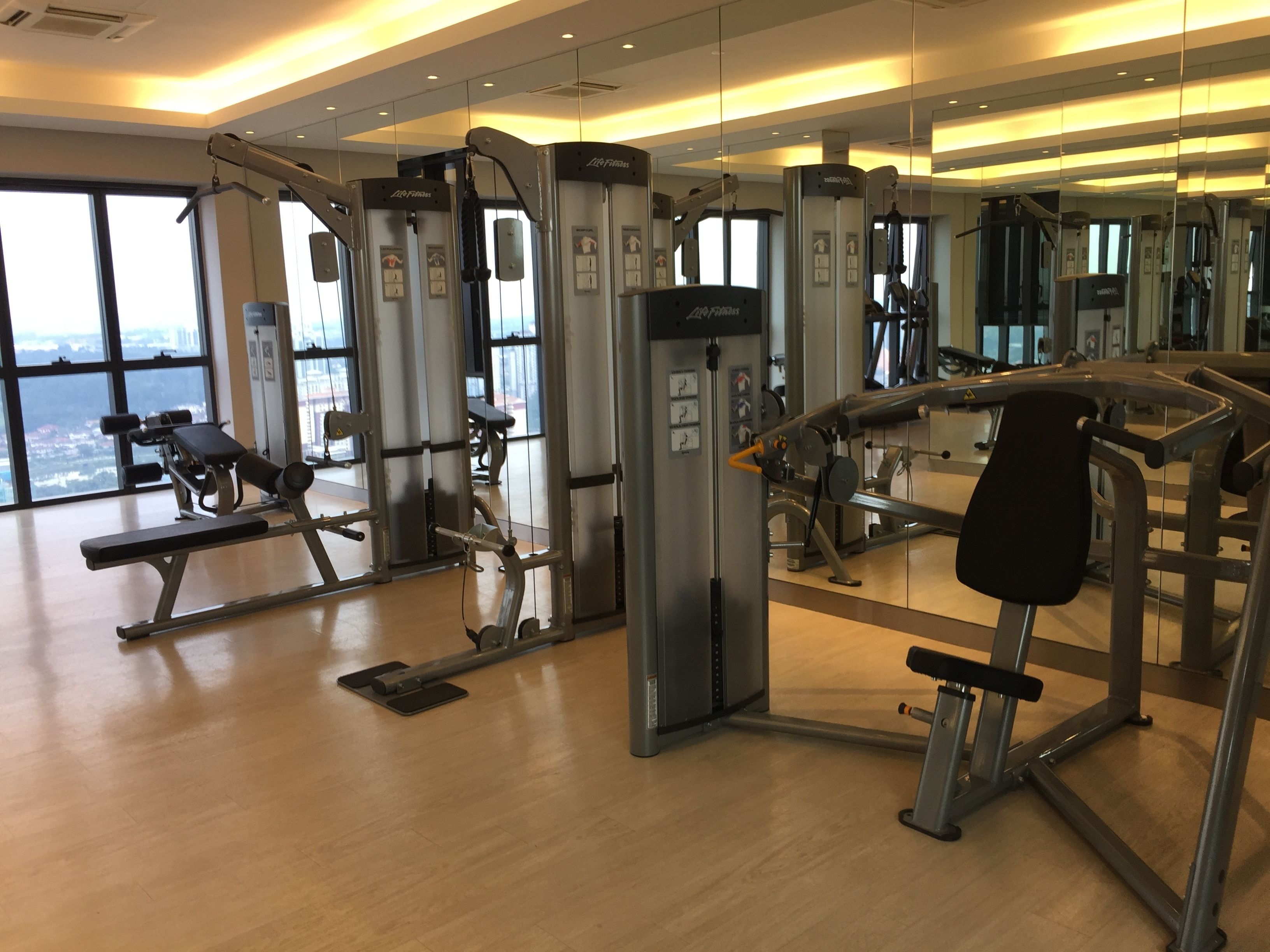 A gym with various exercise machines, large windows, and a view of the city.
