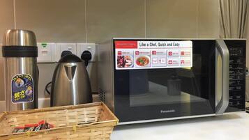Una cocina con un microondas Panasonic, un hervidor de acero inoxidable y una cesta con alimentos.