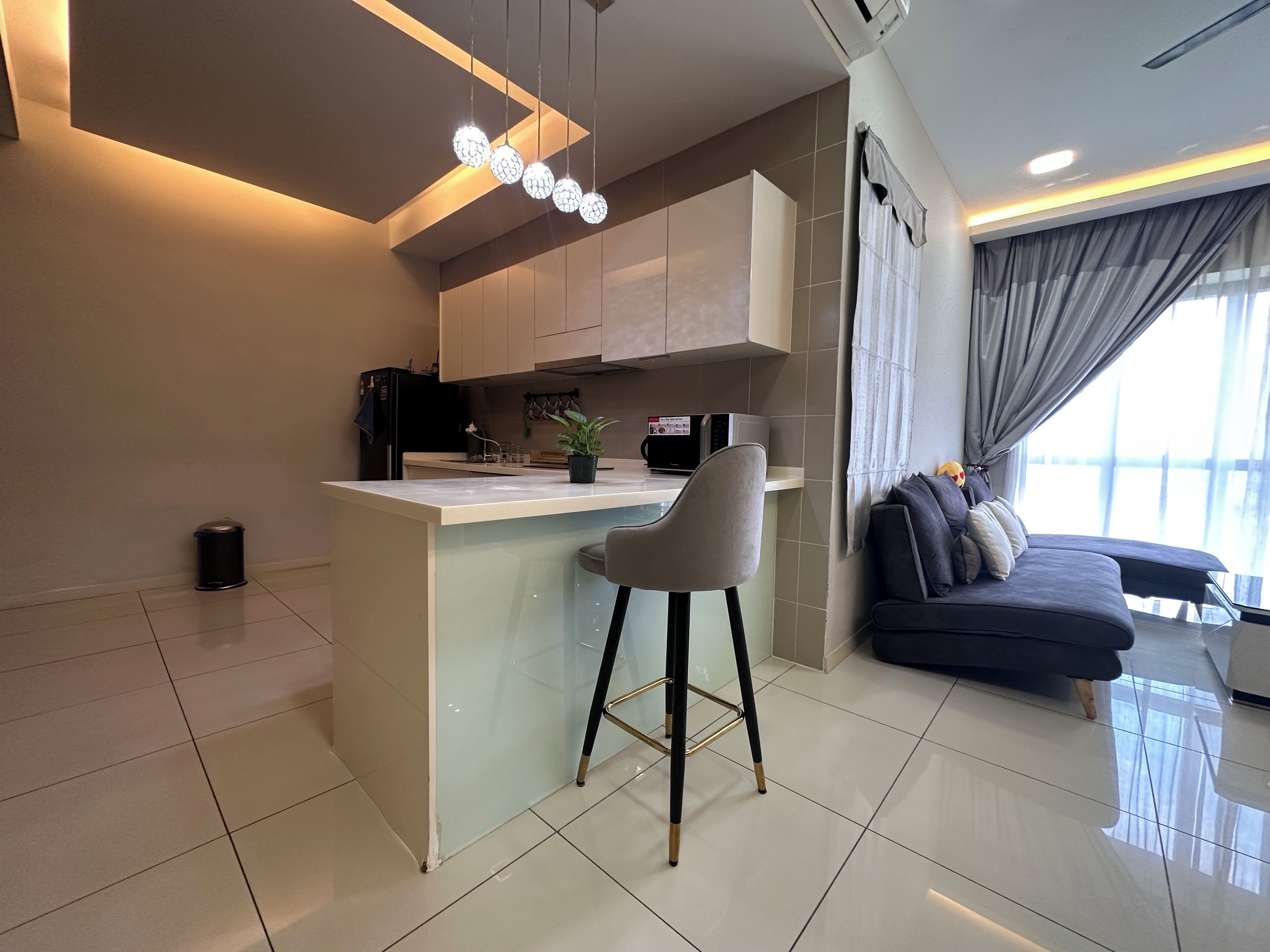 Una cocina moderna con una isla central, taburetes de bar, microondas y una planta en maceta.
