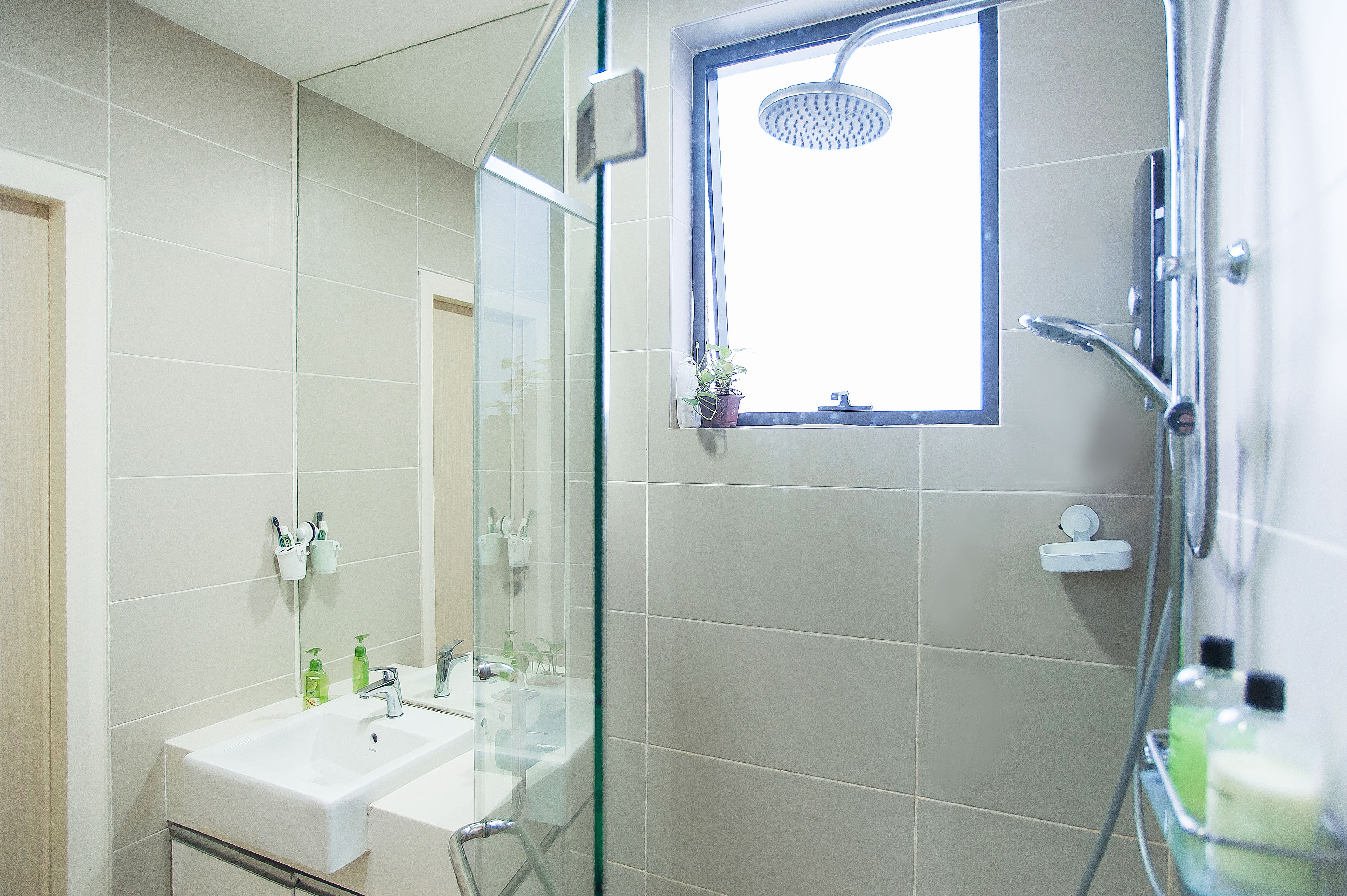 A modern bathroom with a glass shower enclosure, a window, and a sink with toiletries.