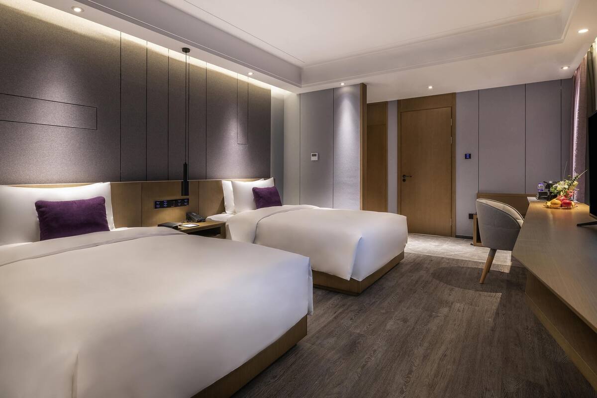 A modern hotel room with two beds, a desk, and a television.