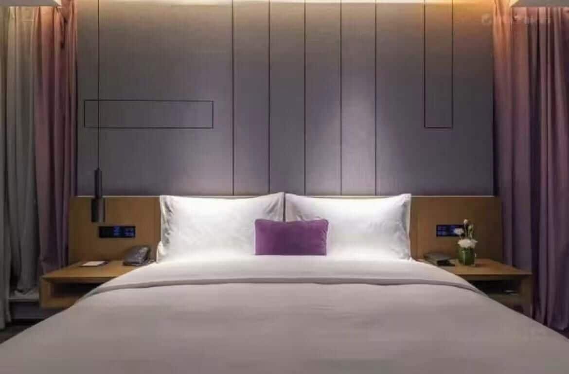 A hotel room with a bed, nightstands, a wall-mounted control panel, and curtains.