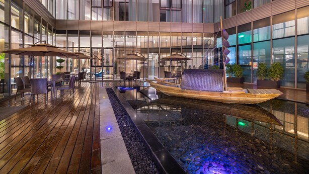 A modern indoor pool area with a boat, lounge chairs, and tables. - Mercure Kunshan MIXC Hi-tech (Suzhou)