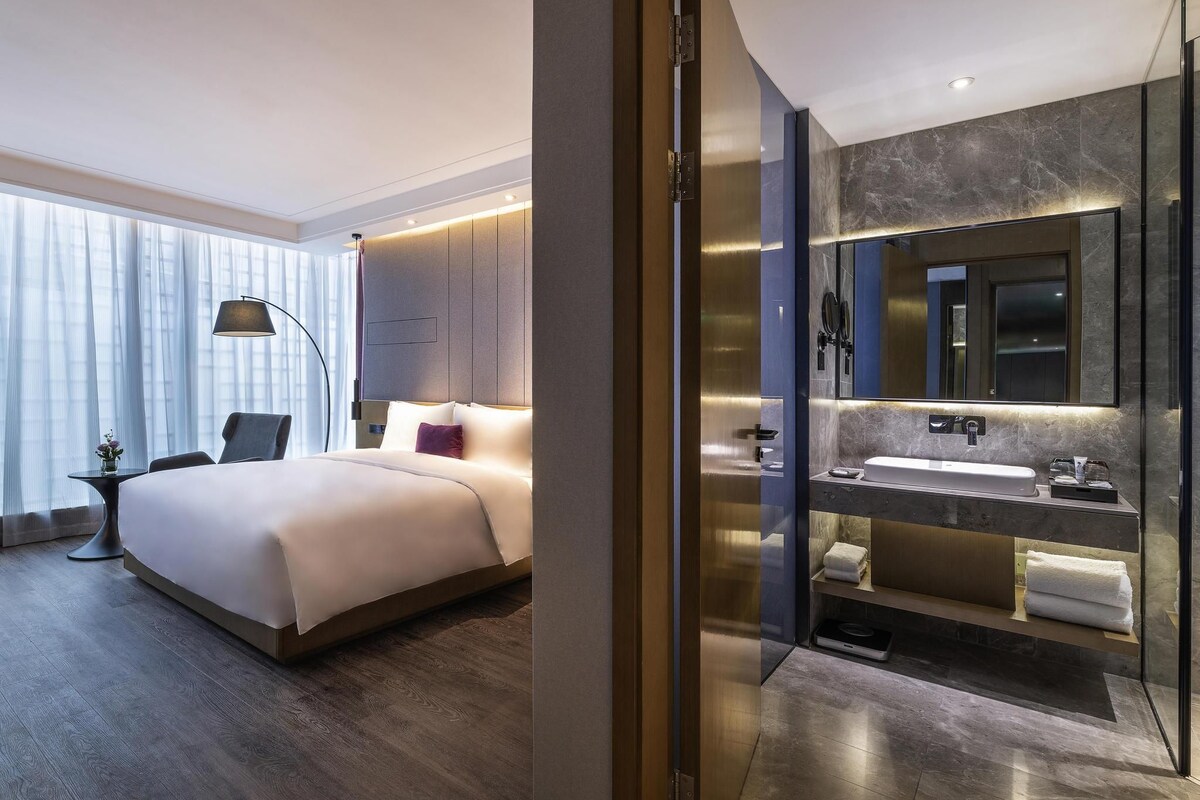 A modern hotel room with a large bed, a separate bathroom with a vanity, and a large mirror.