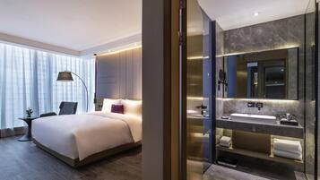 Una habitación de hotel moderna con una cama grande, baño independiente con tocador y un espejo amplio.
