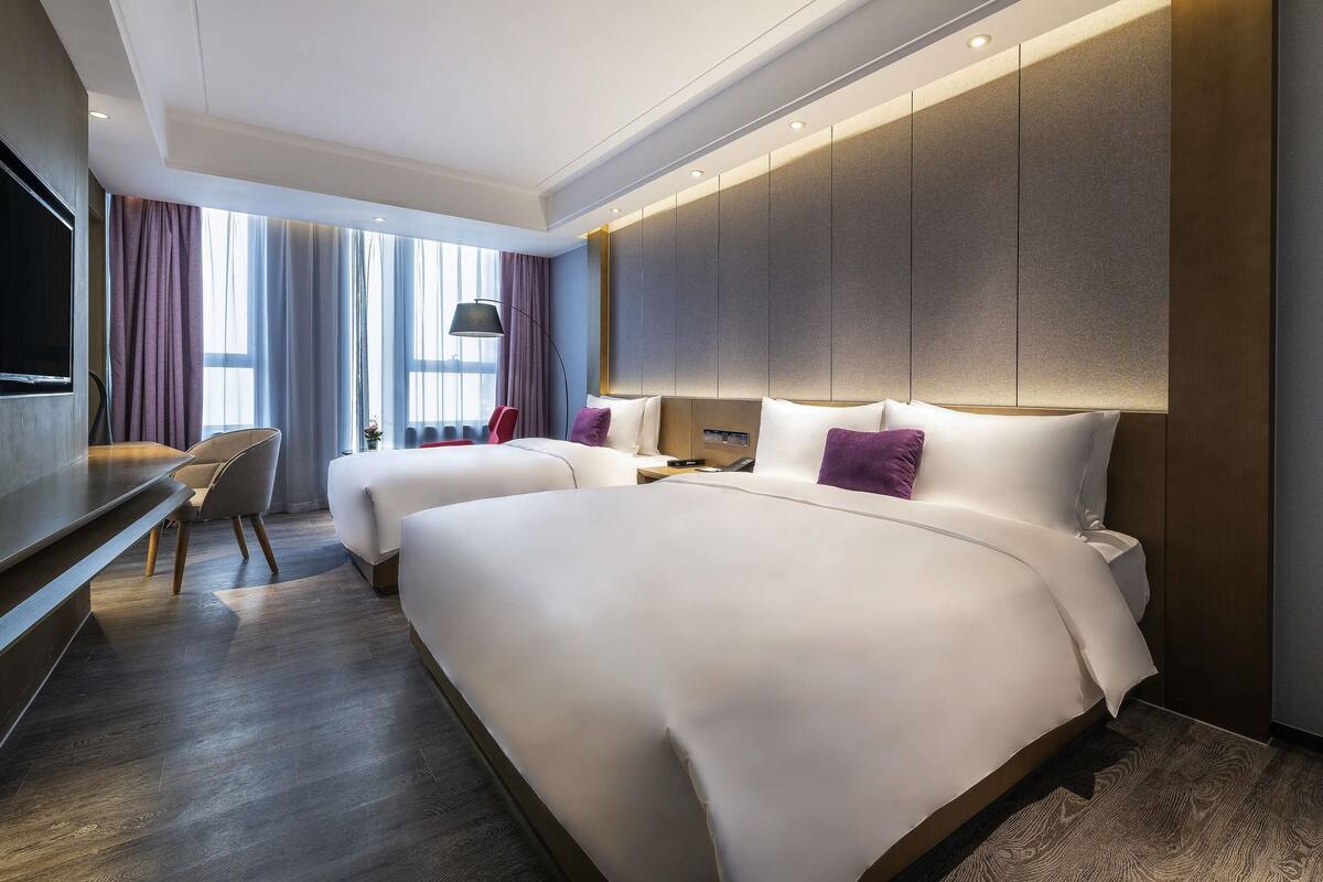A hotel room with two beds, a desk, and a TV.