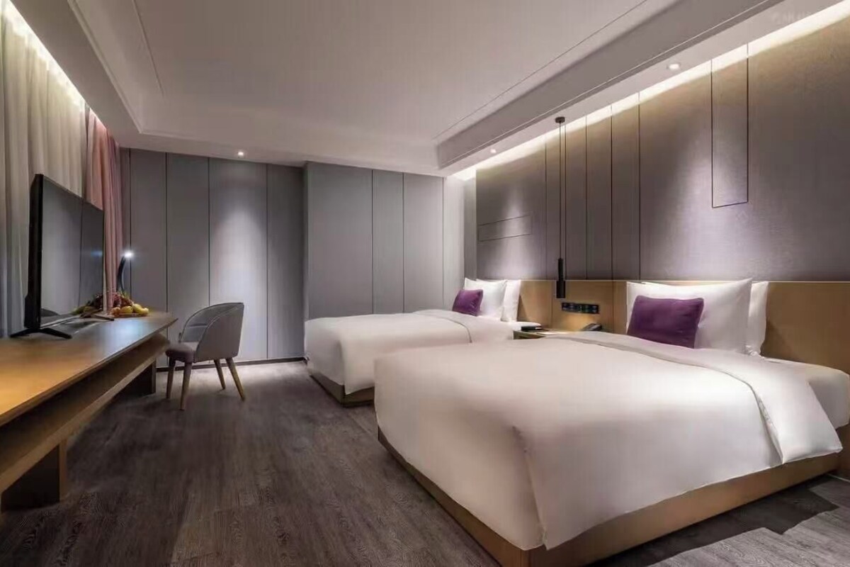 A modern hotel room with two beds, a desk, and a TV.
