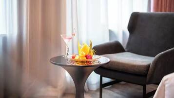 A modern room with a dark grey sofa, a small round table with a martini glass and fruit, and a window with curtains.