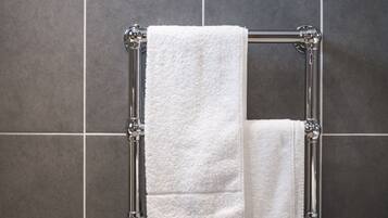 A bathroom with a chrome towel rack holding two white towels against a tiled wall.