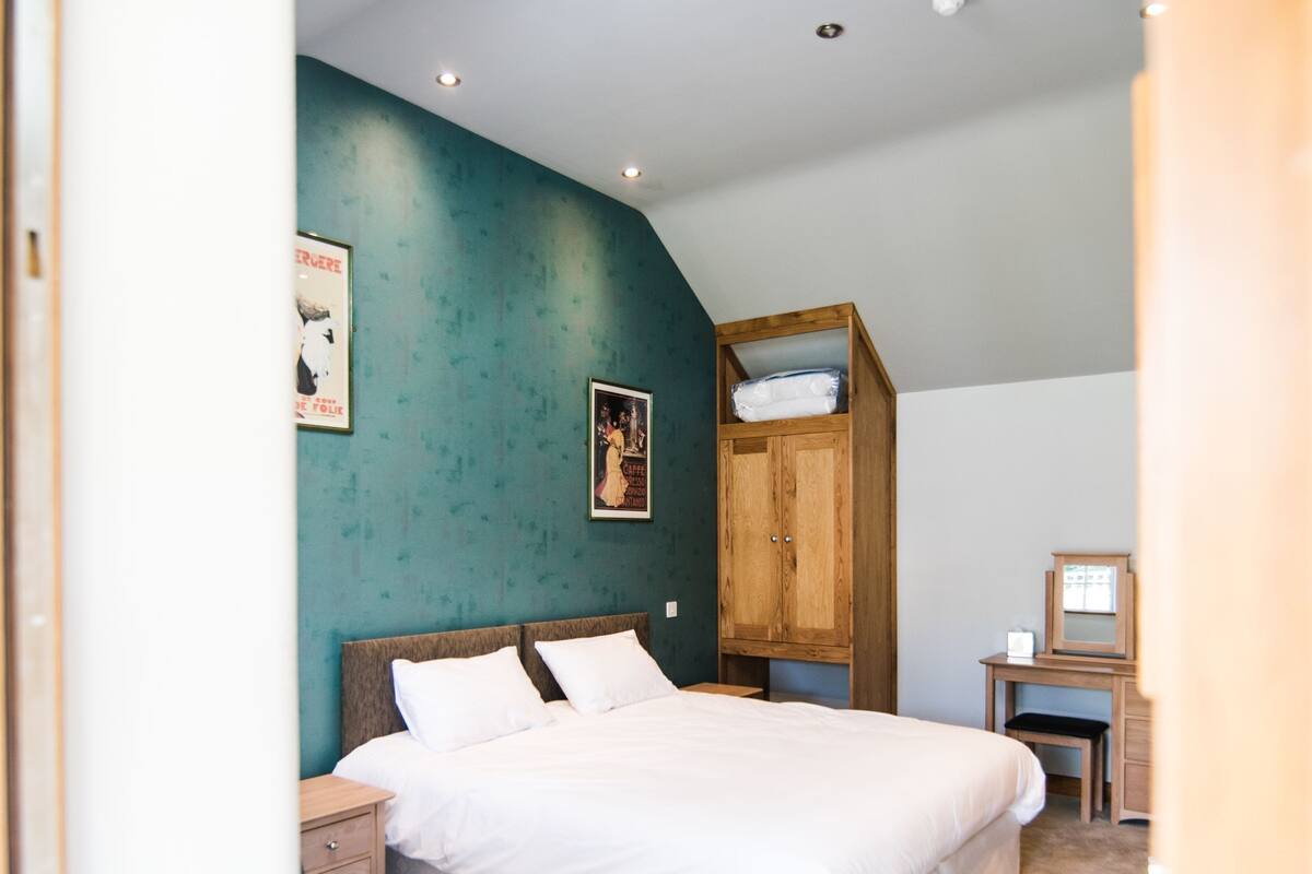 Un dormitorio con una cama, mesitas de noche, un armario de madera y un escritorio con espejo.