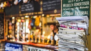 Een bar met een stapel kranten en een bord waarop de Isle of Ely & Wisbech Advertiser wordt aangeboden.