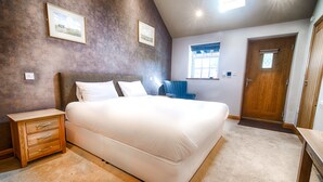 Een slaapkamer met een groot bed, een nachtkastje, een stoel en een deur.