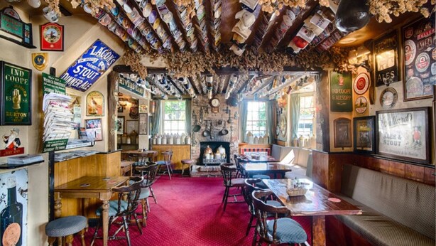 Een pub met houten meubels, een rood tapijt en diverse bierposters op de muren.