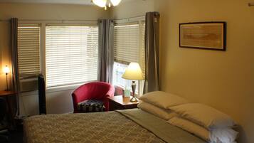 A hotel room with a bed, a red chair, a desk with a lamp, and a ceiling fan.