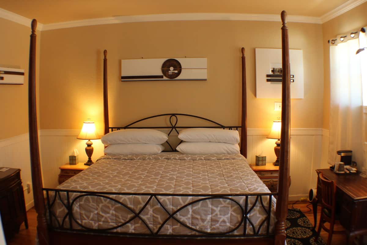 Un lit à baldaquin avec une couvre-lit à motifs, deux lampes de chevet et une horloge au mur.
