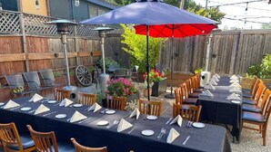 A long dining table set outdoors with multiple chairs, covered with a dark tablecloth, and surrounded by wooden chairs. - San Anselmo Inn (San Anselmo)