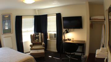 Una habitación de hotel con cama, escritorio, silla, televisor y armario.