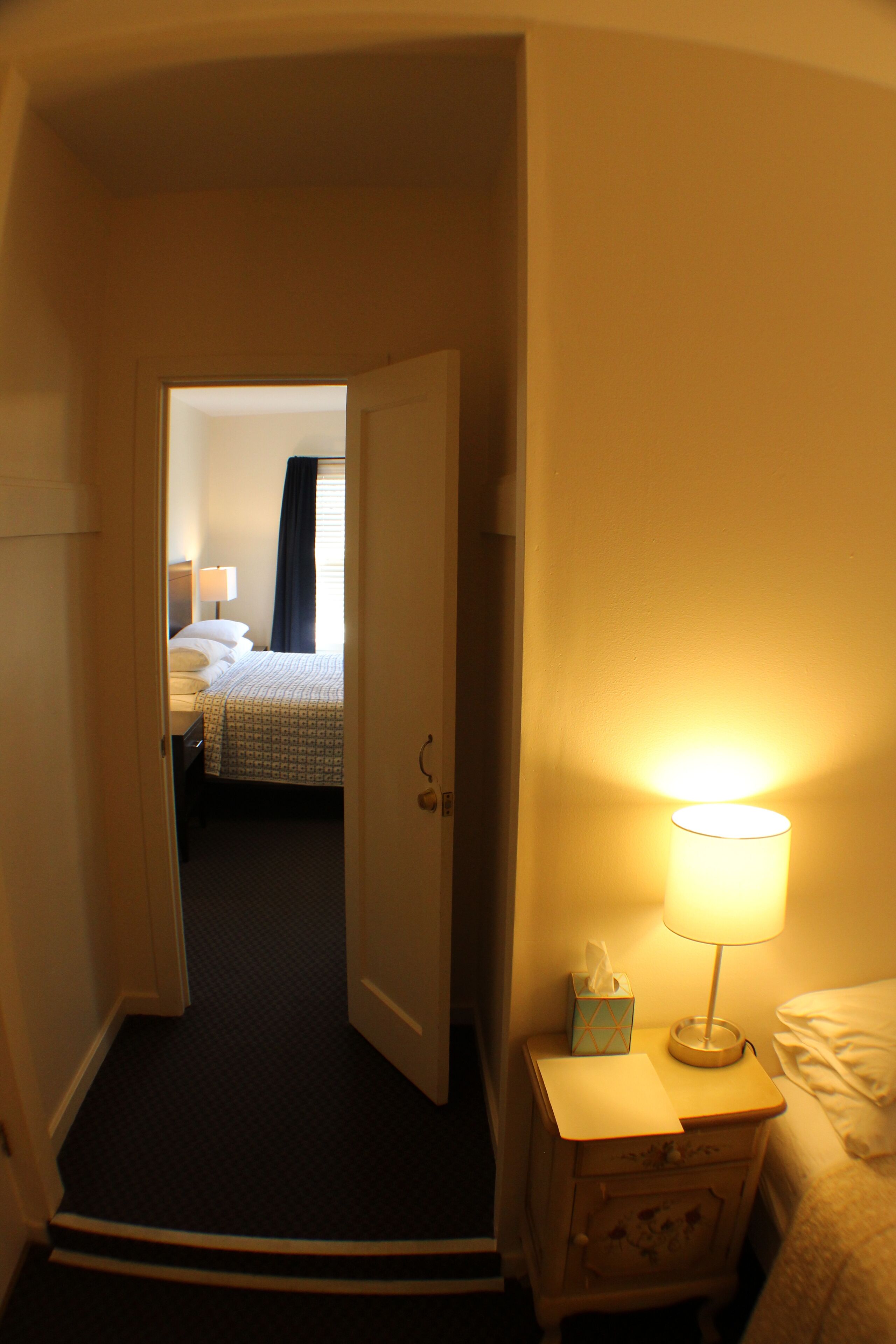 A hotel room with a bed, a bedside table with a lamp, and a nightstand with a tissue box.