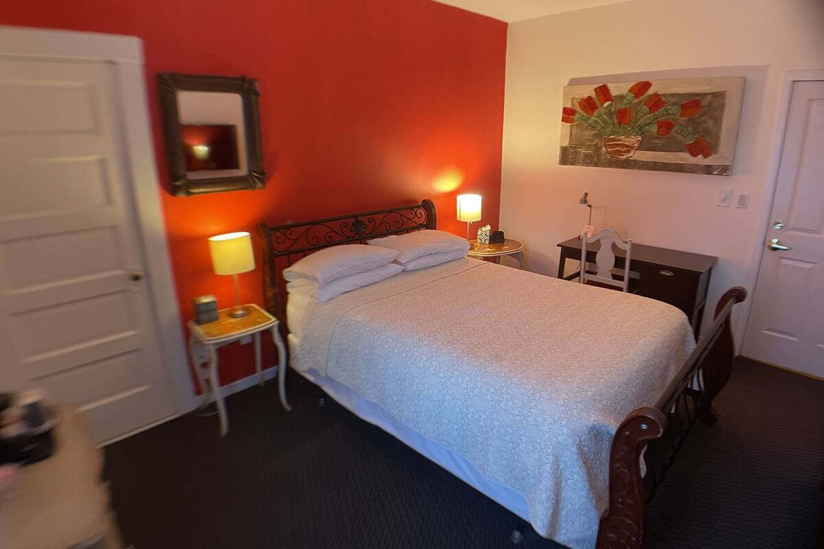 Une chambre d’hôtel avec un lit, des lampes de chevet, une petite table, une chaise, un tableau et une porte.