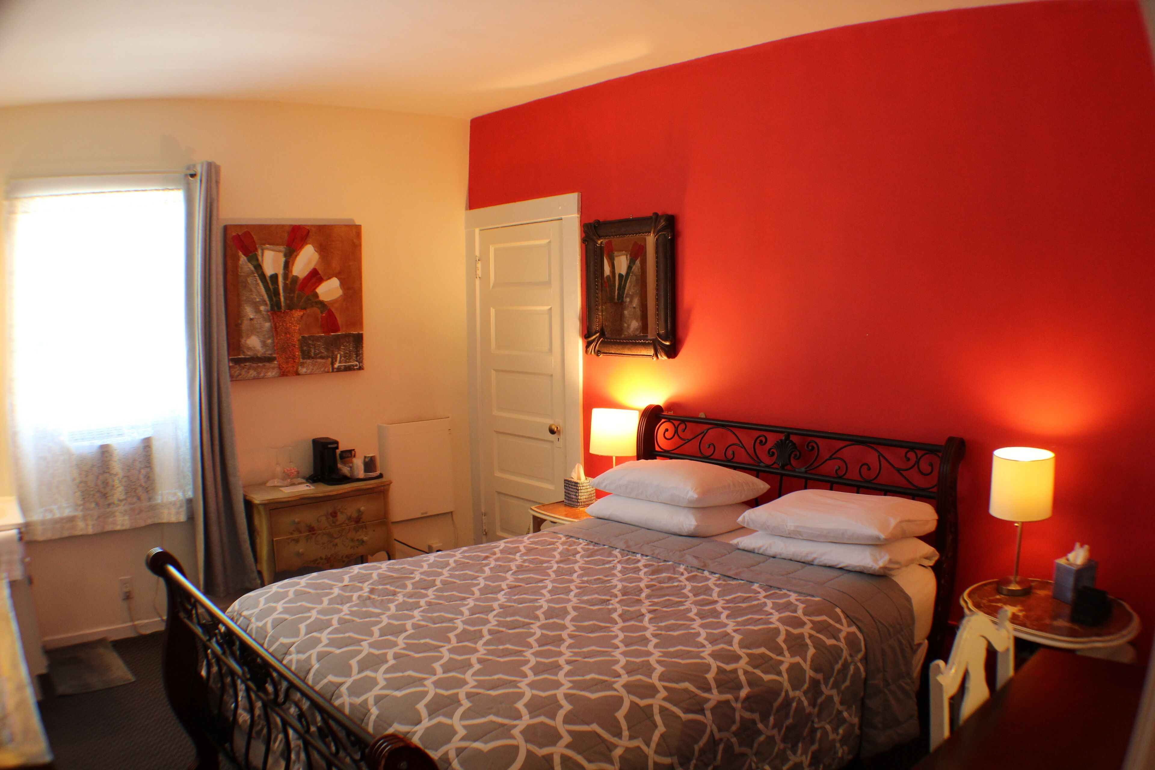 A hotel room with a bed, bedside lamps, a door, and a painting on the wall.