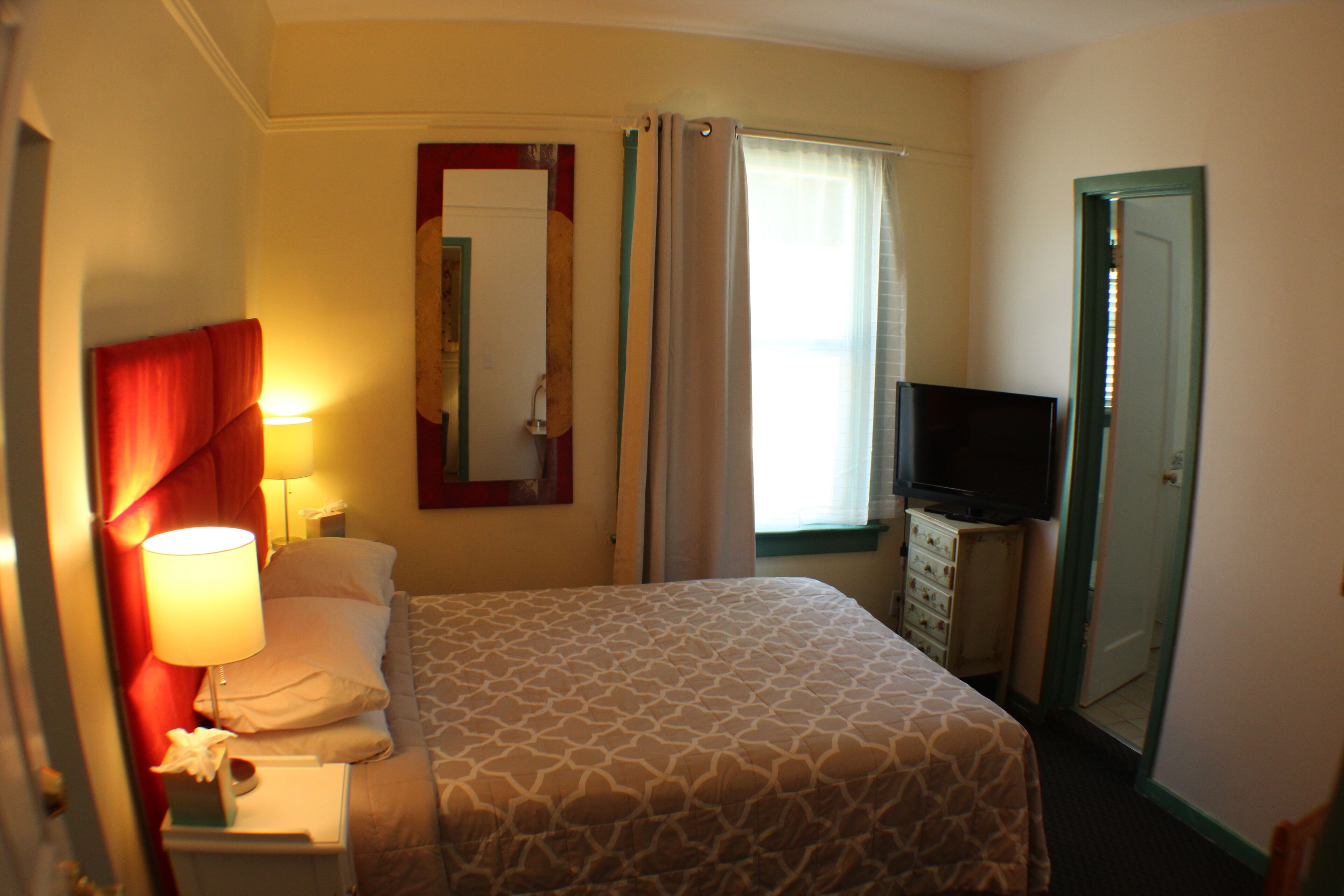 Een hotelkamer met een bed, een televisie, een nachtkastje, een lamp en een spiegel.