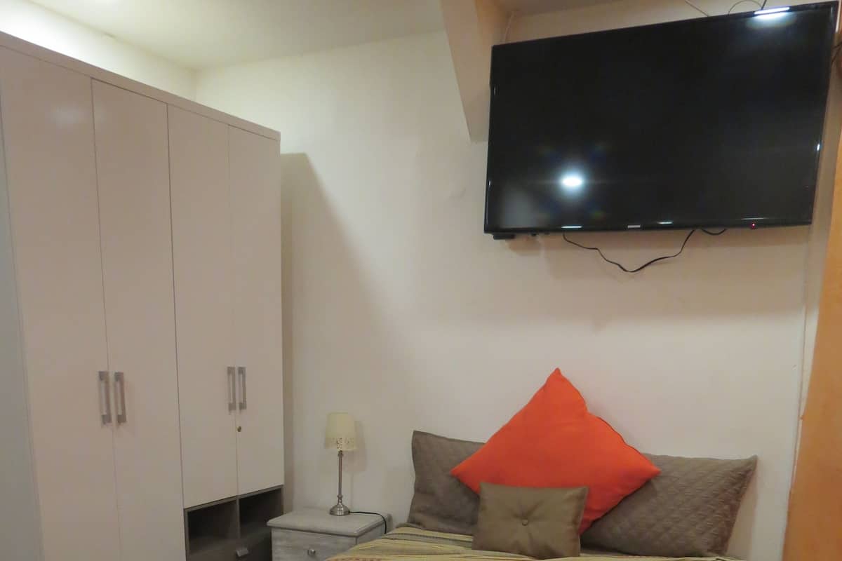 A hotel room with a bed, a TV mounted on the wall, a wardrobe, and a nightstand with a lamp.