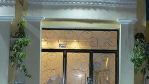 Ein Hotel Eingang mit schmiedeeisernem Tor, einer Leuchte darüber und Pflanzgefäßen an beiden Seiten.