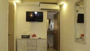 Un baño con tocador, espejo, televisor montado en la pared y aire acondicionado.