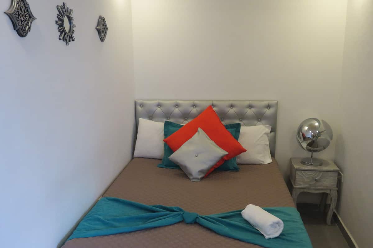 A neatly made bed with a grey headboard, a teal blanket, and a rolled towel.
