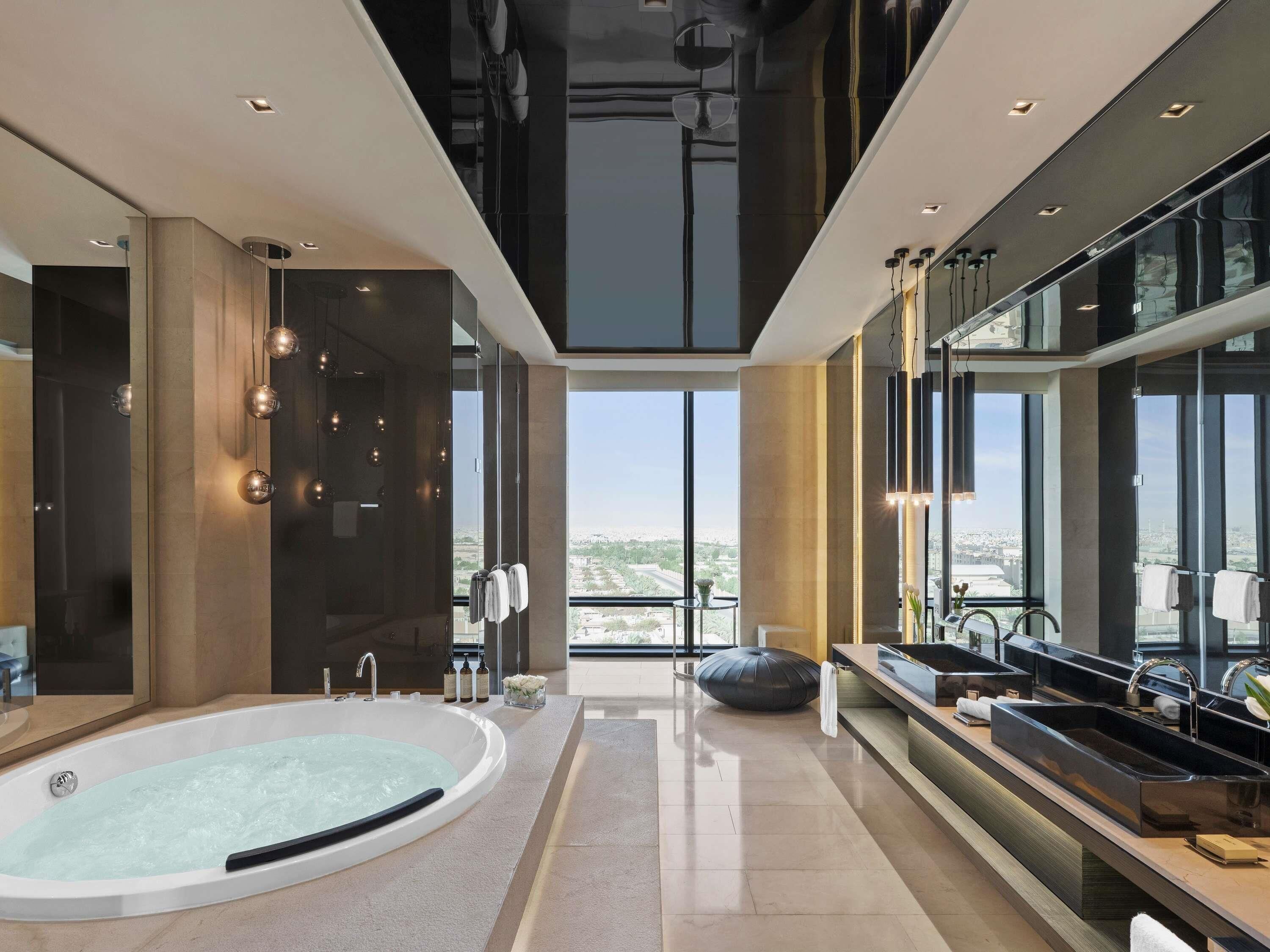 Une salle de bain moderne dotée d’une grande baignoire, d’un meuble-lavabo avec plusieurs vasques et de grandes fenêtres offrant une vue sur la ville.