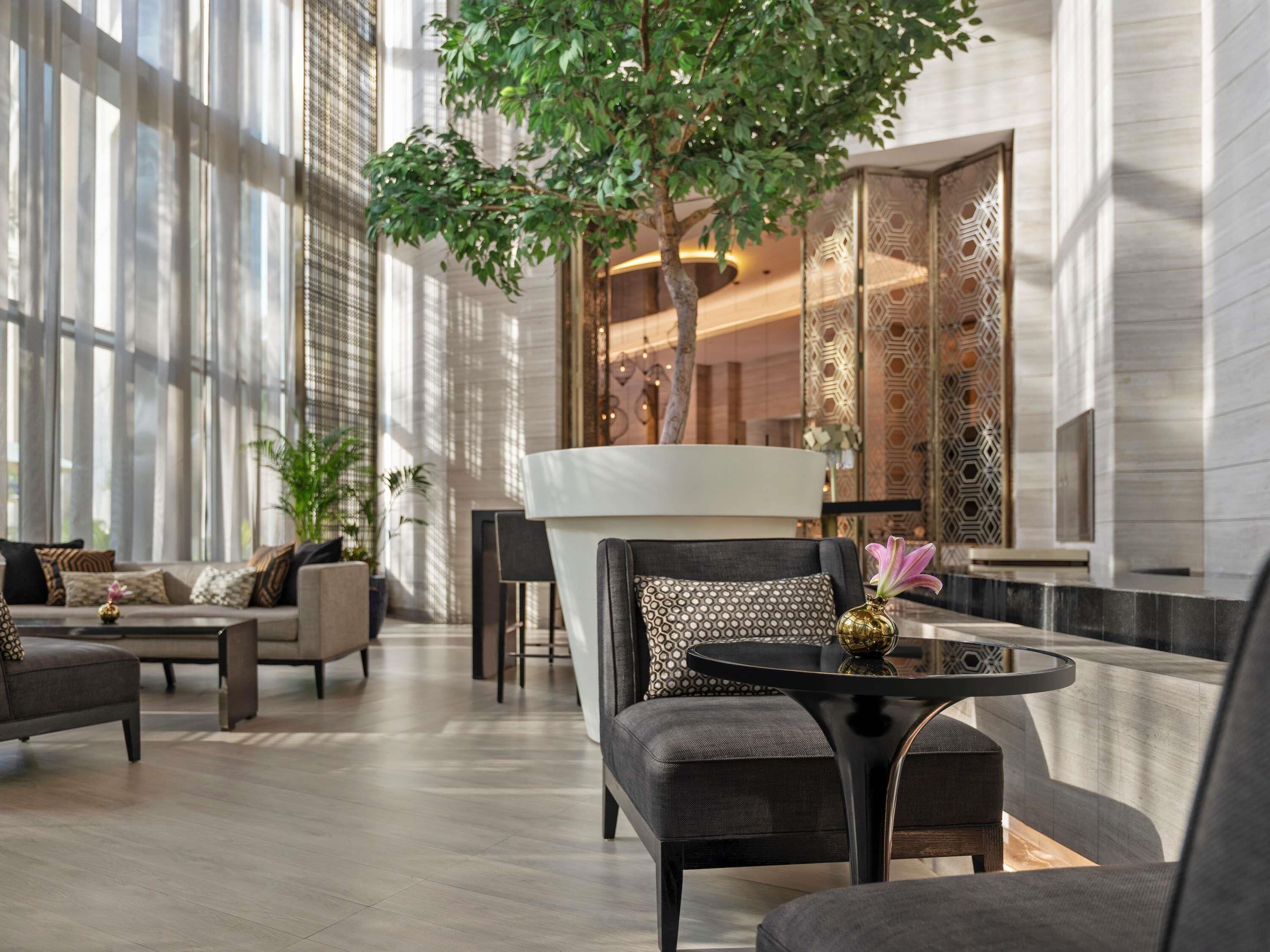 A modern hotel lobby with a large tree, comfortable seating, and a decorative wall.