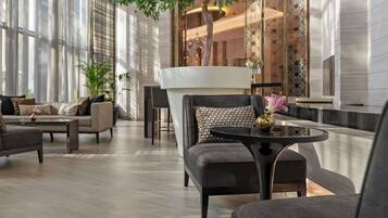 A modern hotel lobby with a large tree, comfortable seating, and a decorative wall.