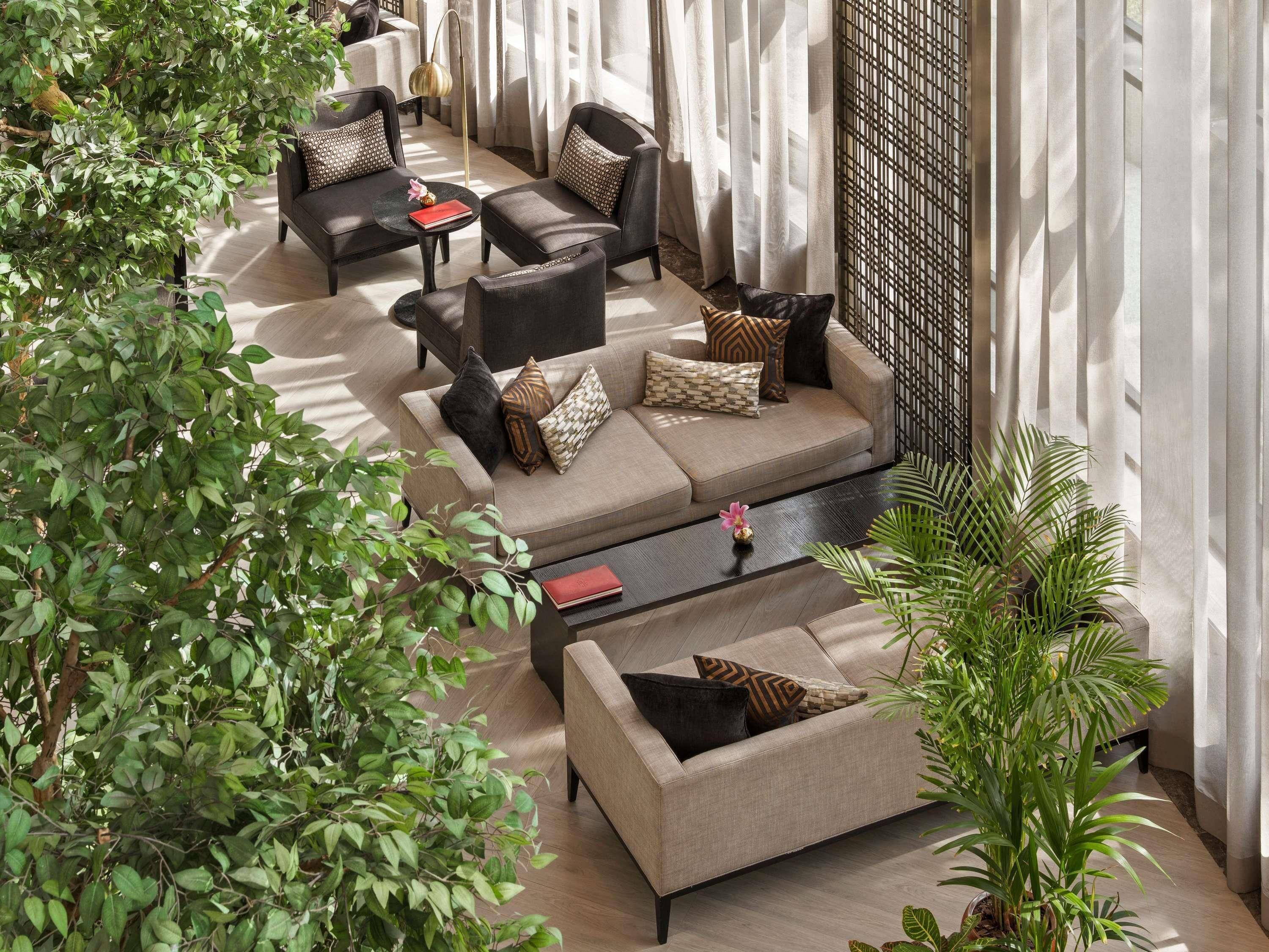Un área de estar moderna con sofás y sillones, una mesita de centro y abundante vegetación.