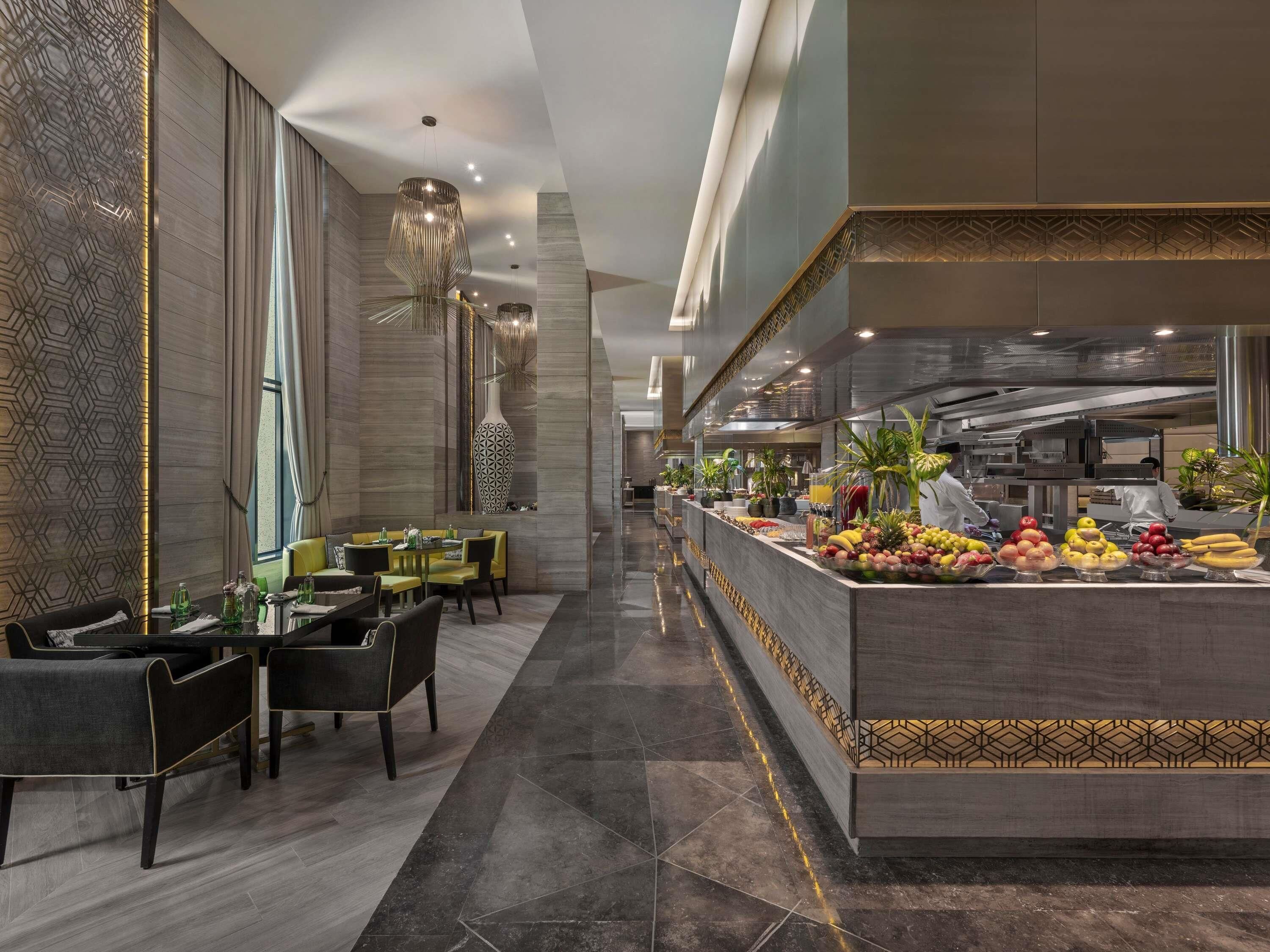 Un moderno vestíbulo de hotel con una larga recepción, una zona de estar y vistas a la cocina.
