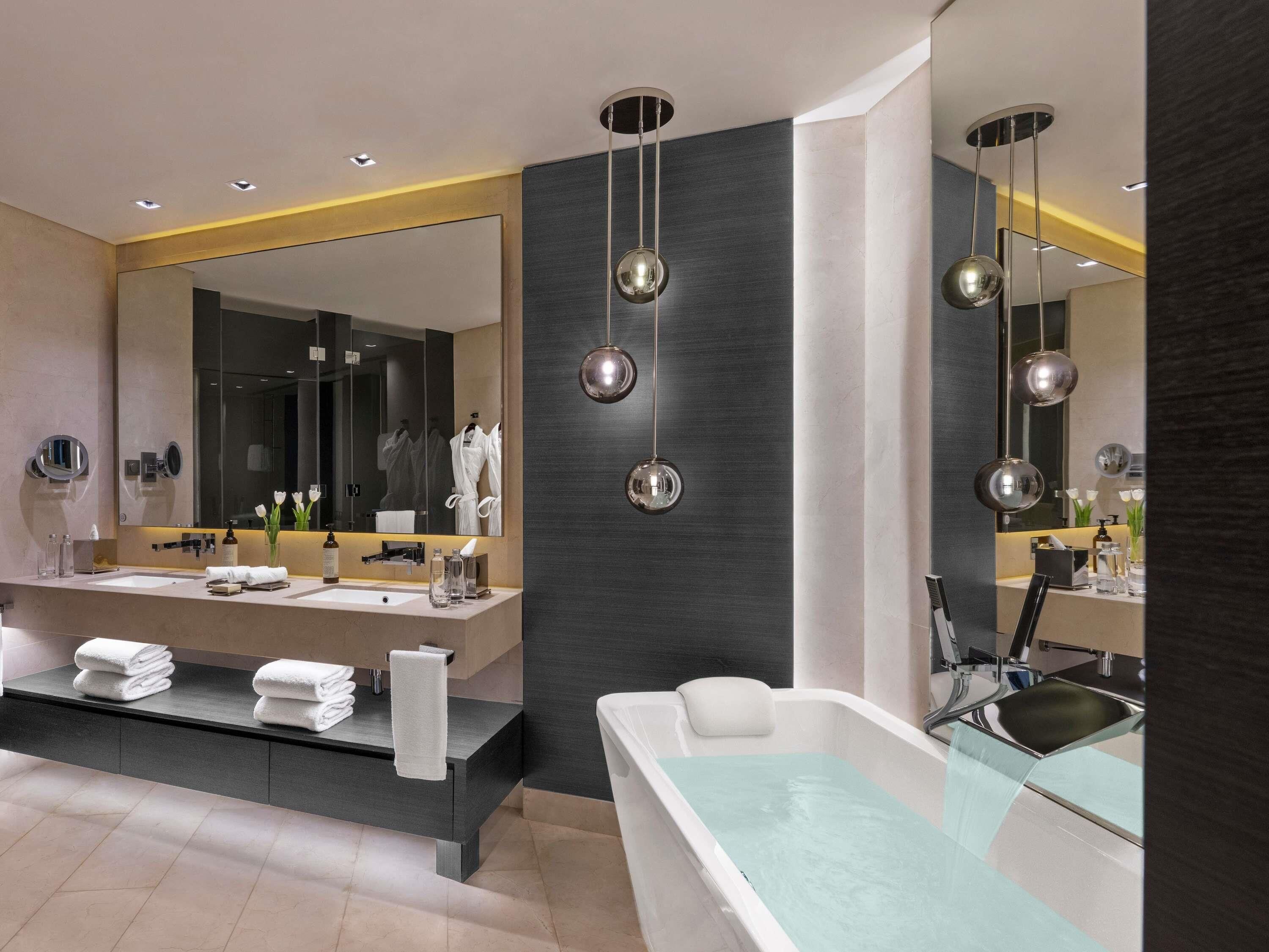 A modern bathroom with dual sinks, a large mirror, and a freestanding bathtub.