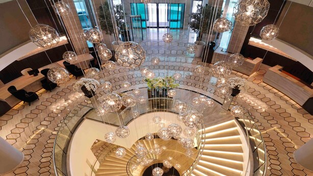 A modern hotel lobby with a central spiral staircase, hexagonal patterned flooring, and hanging crystal chandeliers. - Fairmont Riyadh (Riyadh)