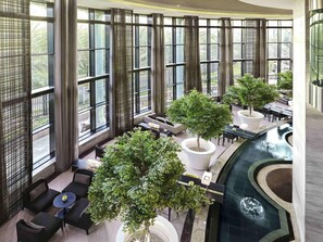 A spacious indoor area with large windows, seating arrangements, and potted trees. - Fairmont Riyadh (Riyadh)