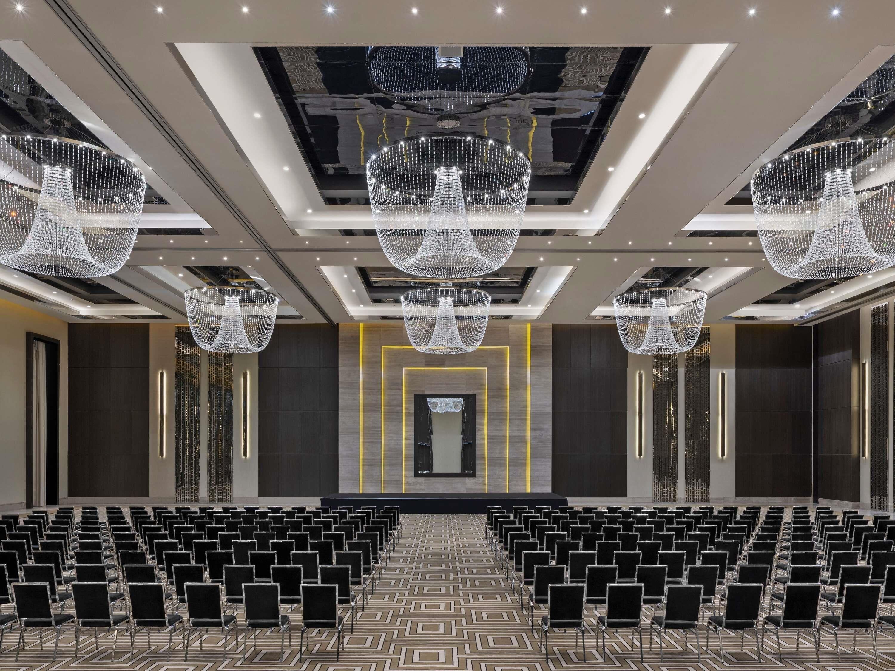 A conference room with rows of chairs, a stage, and large chandeliers.