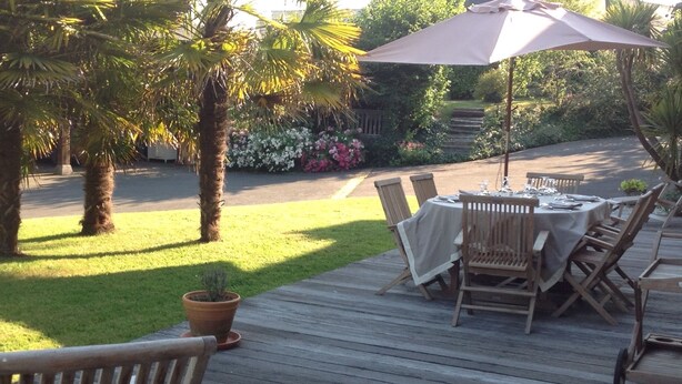 An outdoor dining area with a wooden deck, a table set with chairs, and a potted plant. - La Peuterne (Mouazé)